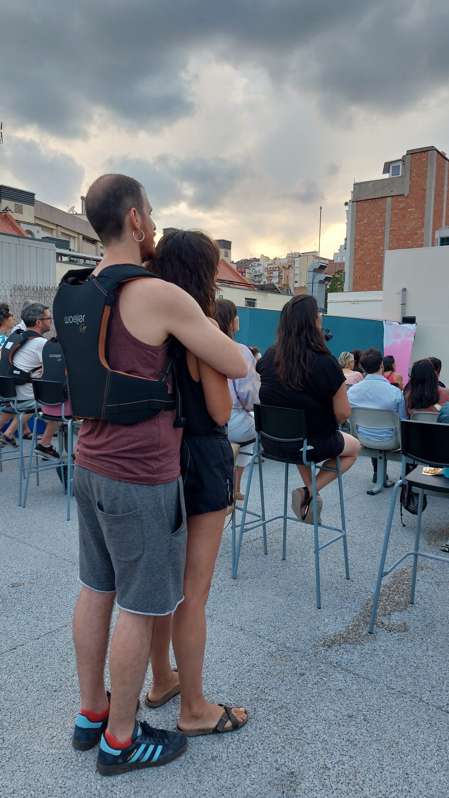 Parella abraçada mirant un espectacle de Terrats en Cultura a l’aire lliure amb motxilla vibratòria per seguir la música.