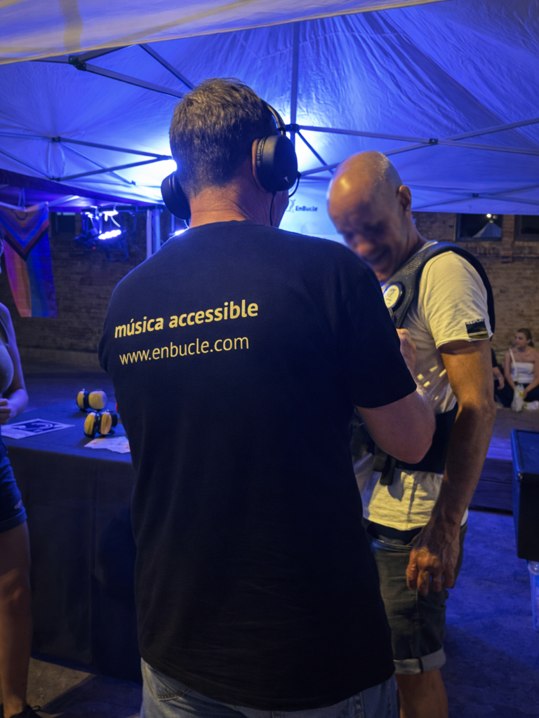 Persona provant una motxilla vibratòria amb l’ajuda d’un tècnic d’EnBucle en un espai exterior nocturn, amb il·luminació blava i taula amb equips d’accessibilitat al fons.