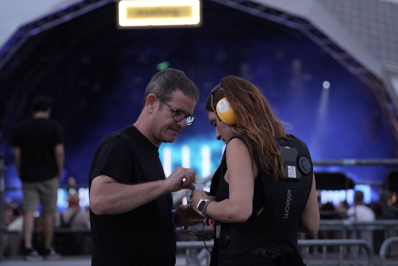 Persona utilitzant motxilla vibratòria en un concert al Festival Cruïlla mentre rep assistència per ajustar l’equip.
