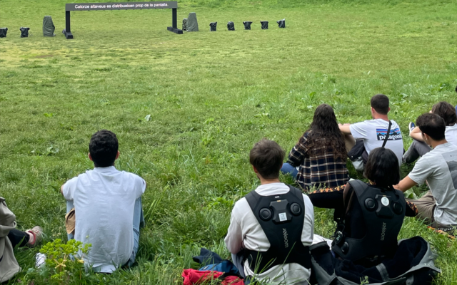 Públic assegut a l’aire lliure amb motxilles vibratòries durant un espectacle al festival Sismògraf.