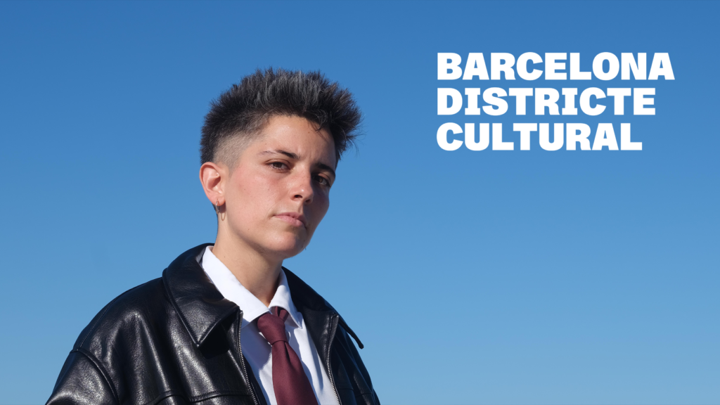 Retrat de l’artista OKDW sobre fons blau, amb el text «Barcelona Districte Cultural».
